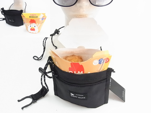 黒いネックストラップポーチに「からあげクン」の容器がぴったりと収まっている様子。ポーチはマネキンの首にかけられ、手前にはペットボトルホルダーがぶら下がっています。背景には別の「からあげクン」の箱が小さく写っています。このポーチが「からあげクン」のサイズに特化していることを示唆する画像です。
